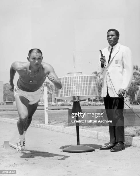 Full-length image of Olympic decathlon hopeful, C.K. Yang , leaving a starting block as 1960 decathlon gold medal winner Rafer Johnson stands by with...