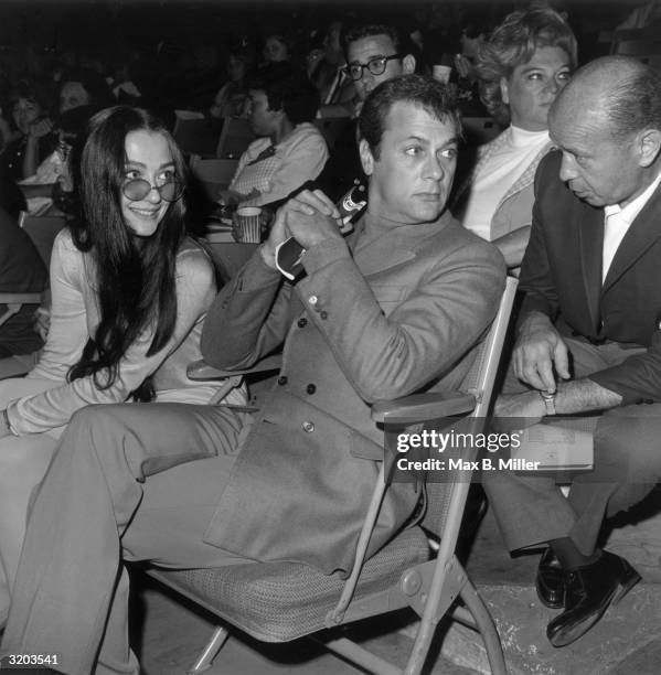 American actor Tony Curtis sitting with his wife, Austrian-born actor Christine Kaufmann, in the audience at singer Bobby Darin's opening at...