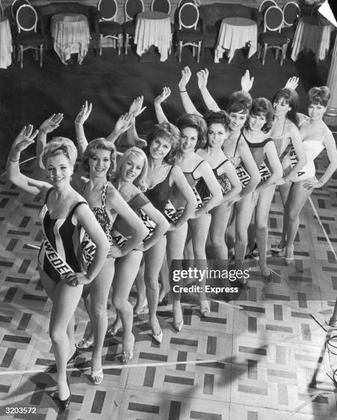 Full-length group portrait, taken from above, of Miss Circlorama finalists from around the world, waving in swimsuits on the dance floor at the Cafe...