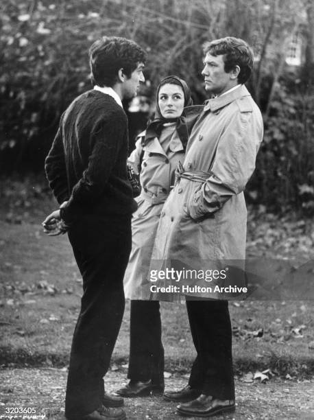 Full-length image of British director Stephen Frears talking with French actor Anouk Aimee and her husband, British actor Albert Finney, outdoors on...