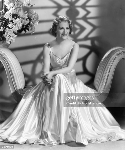 British singer and comedian Gracie Fields , wearing a long silk evening gown, sits on a divan in a promotional portrait for director Monty Brooks'...