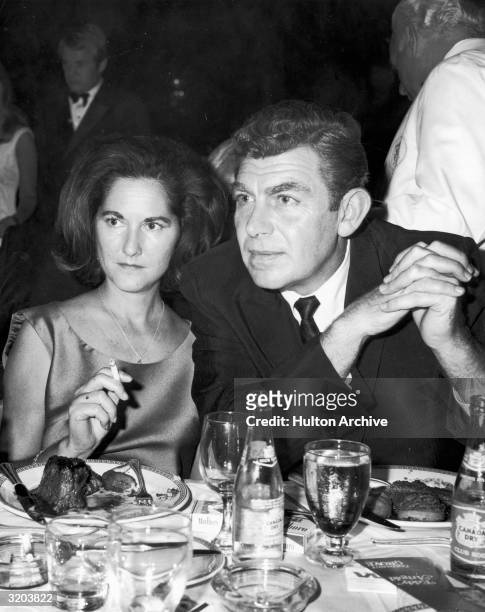 American actor Andy Griffith sits at a restaurant table with his first wife, Barbara Edwards. She holds a cigarette. They have meals on their plates,...