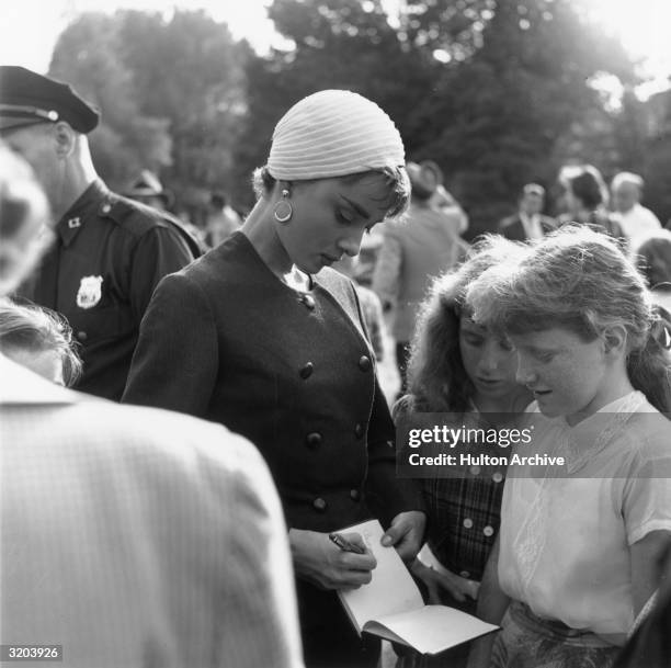 Belgian-born actor Audrey Hepburn signs an autograph book for two young girls on the set of director Billy Wilder's film, 'Sabrina'. Hepburn wears a...