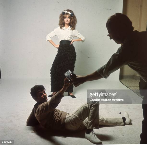 British model Jean Shrimpton poses for a shoot while American photographer Richard Avedon lays on the floor, taking a camera from an assistant....