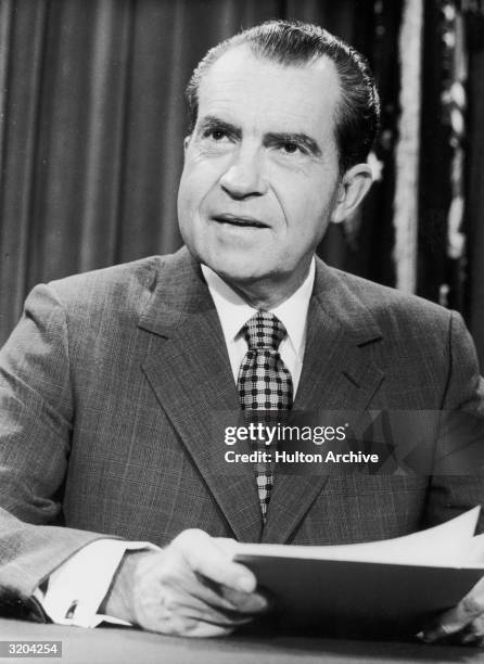 President Richard M. Nixon smiles and holds papers while seated at a desk.