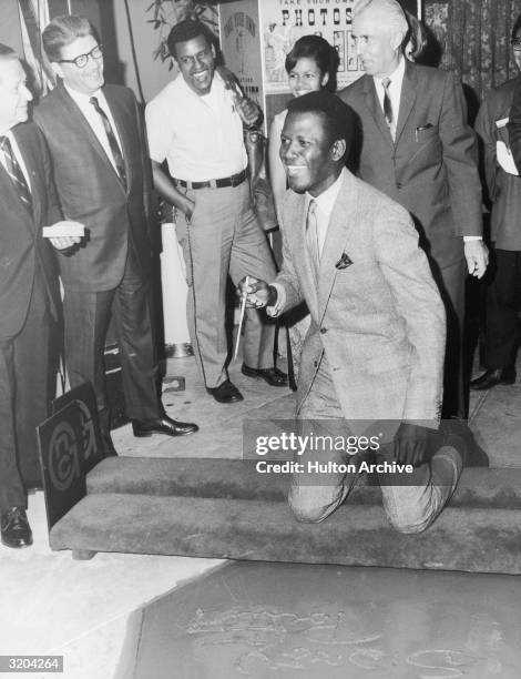 American actor Sidney Poitier kneels in front of his name, just signed in the wet cement at Grauman's Chinese Theatre, Hollywood, California.