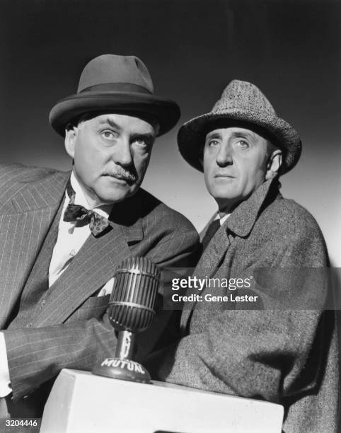 Studio portrait of British actor Nigel Bruce and South African-born actor Basil Rathbone posing behind a microphone. Both are dressed in character:...