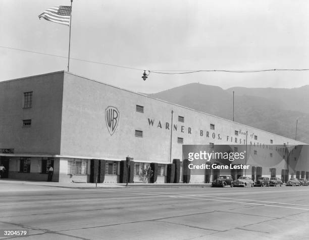 Exterior view of the long concrete building housing Warner Bros. First National Pictures, Los Angeles, California. A U.S. Flag flies from the corner...