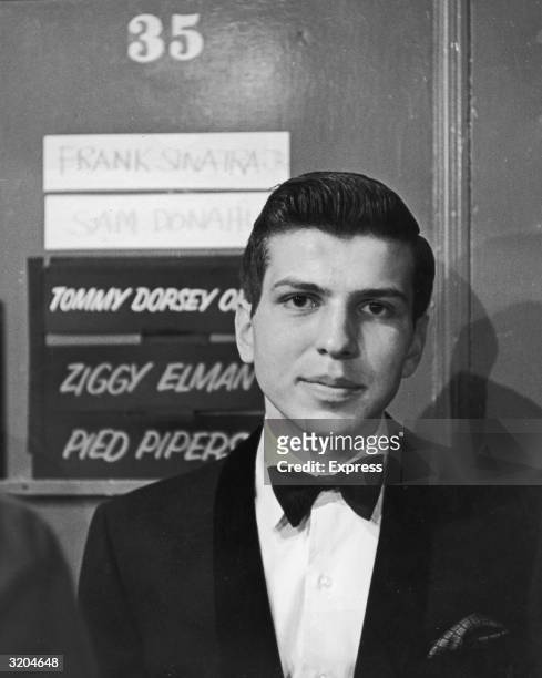 Headshot of American vocalist Frank Sinatra Jr. Wearing a tuxedo while standing in front of the dressing room door he shared with other performers at...