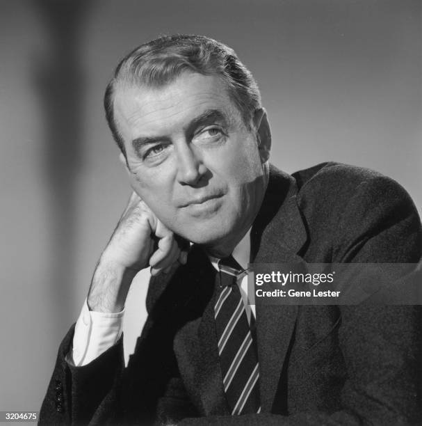 Studio portrait of American actor James Stewart leaning his face against his hand in a jacket and rep tie.