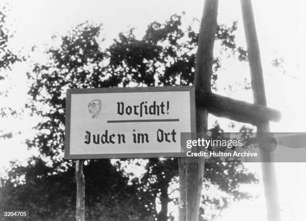 An anti-Semitic sign, written in German, indicating a Jewish area and including a caricature of a Jew. The sign warns 'Vorsicht! Juden Im Ort' .
