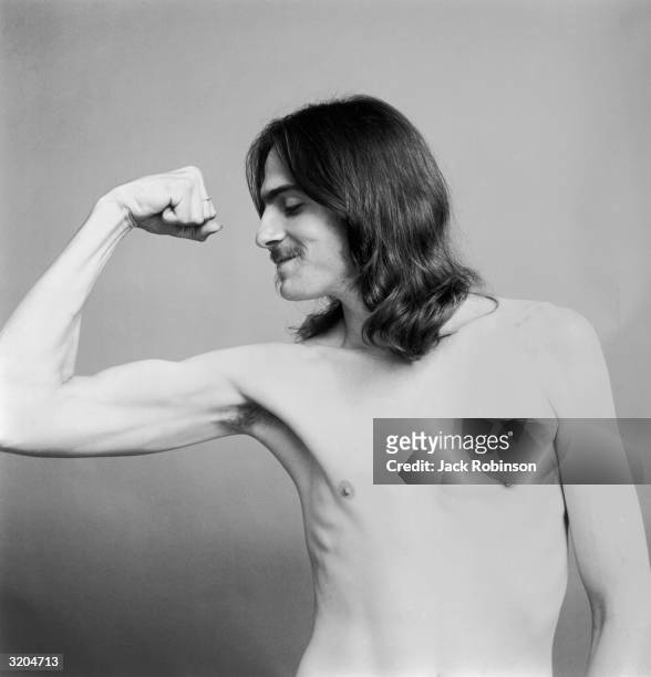 Portrait of American folk musician James Taylor making a muscle with his right arm, bare chested.