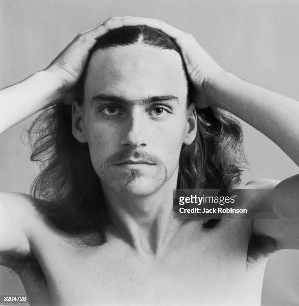 Headshot portrait of American folk musician James Taylor pulling his hair back with his hands. He is bare chested.