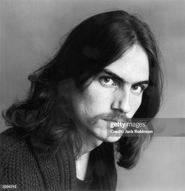 Headshot portrait of American folk musician James Taylor looking at the camera, wearing a black sweater.