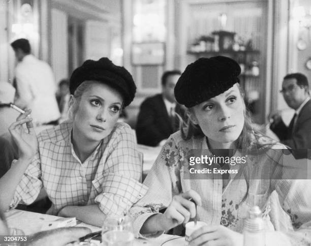 French actor Catherine Deneuve and her older sister, actor Francoise Dorleac , sit in a cafe in a still from director Jacques Demy's film, 'Les...
