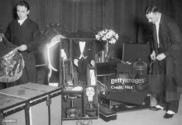 Full-length image of two performers unloading props, including a ventriloquist's dummy, a birdcage, a tea set and flowers, on a stage in front of a...