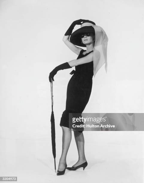 Belgian-born actress Audrey Hepburn in a black cocktail dress designed by French couturier Hubert de Givenchy in a promotional portrait for director...