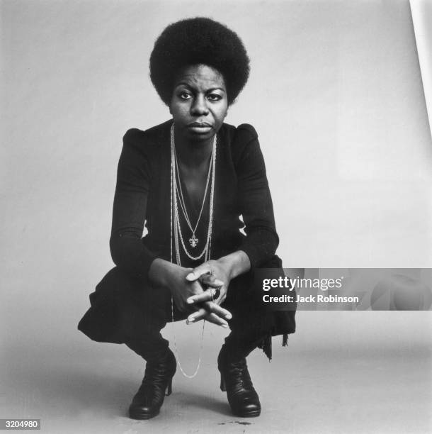 Full-length studio portrait of American vocalist Nina Simone kneeling with her hands folded.