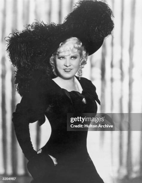 Mae West wears a period costume, including a large hat with trimmed with ostrich feathers, in a promotional portrait for director A. Edward...