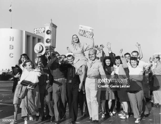 Full-length image of a group of men and women rejoicing in front of the NBC studios on V-J Day at the end of World War II. Some of the women are...
