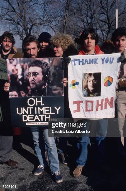 People gathered at Central Park, New York, to mourn the death of John Lennon. They are holding pictures of Lennon.