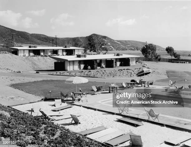 View of an outdoor swimming pool and hotel rooms at the Treasure Island Trailer Park in Laguna Beach, California. Beach chairs and tables surround...