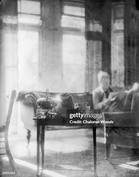 An atmospheric picture of a man reading a newspaper while a table set with tea things stands in the sunny foreground.