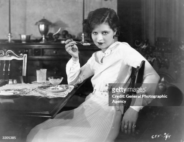 American actress Clara Bow pauses with a spoonful of pudding halfway to her lips.