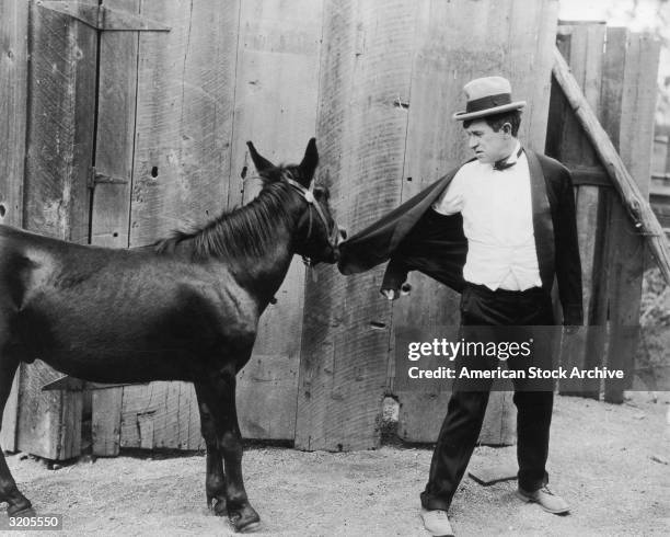 American actor and humorist Will Rogers looks behind as a mule bites his jacket in an unidentified film still.