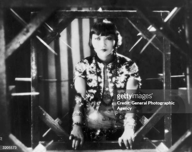 American film star, Anna May Wong framed by a sinister-looking contraption in a still from one of her films.