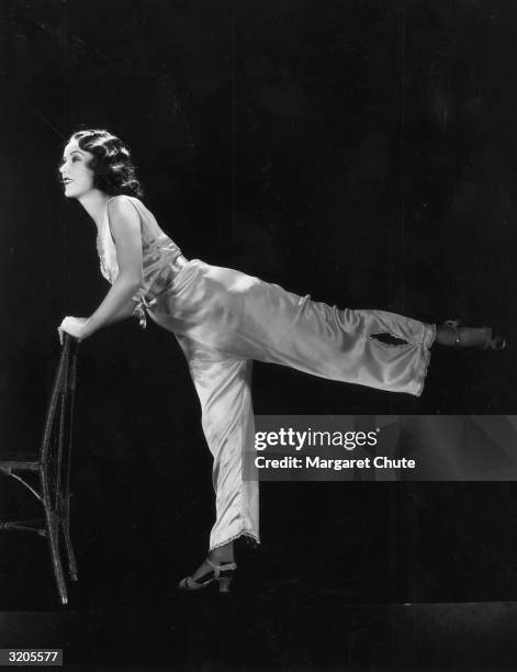 Hollywood film star, Fay Wray leans on a chair to perform 'chorus routine' slimming exercises involving high kicks and stretching.