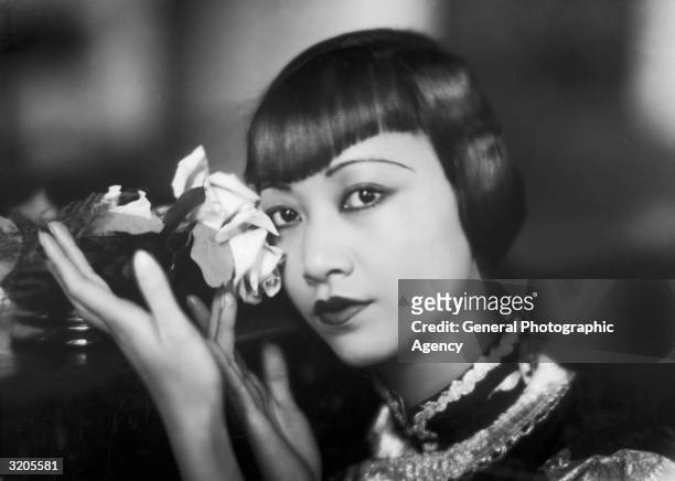 American film star, Anna May Wong poses with a cut rose.