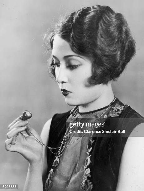 Hollywood film star, Dorothy Sebastian checks the time on a small jade watch worn on a gold and jade chain around her neck.