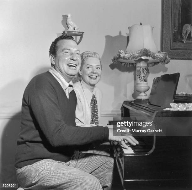 American actor and bandleader Phil Harris laughs as he sits and plays piano with his wife, actor and singer Alice Faye, at their home in Encino,...