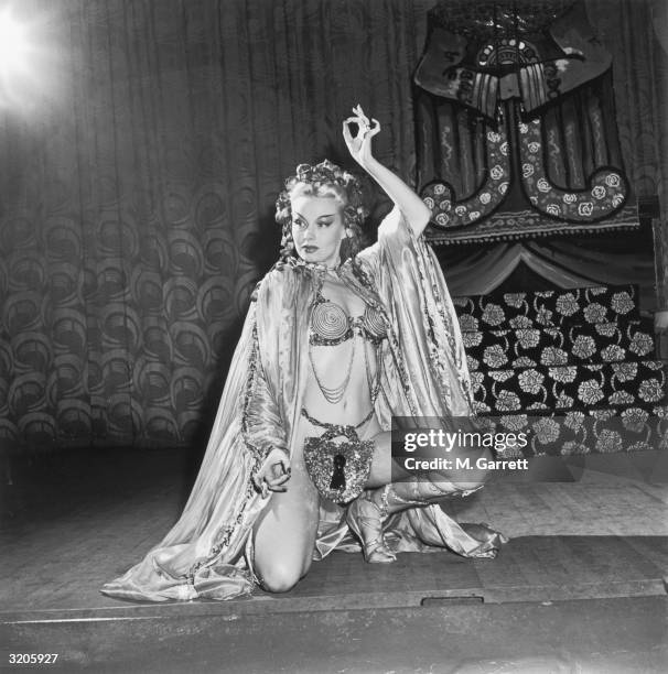 Full-length image of American exotic dancer Lili Saint Cyr kneeling in a pose with one arm up, at the Follies Theatre in Los Angeles, California. St....