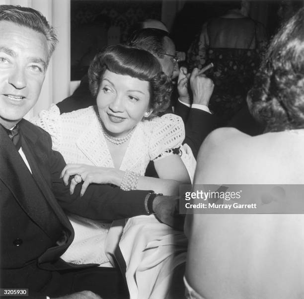 French-born actor Claudette Colbert sits with her husband, Dr. Joel Pressman, while attending actor Betty Hutton's party to celebrate the wedding of...