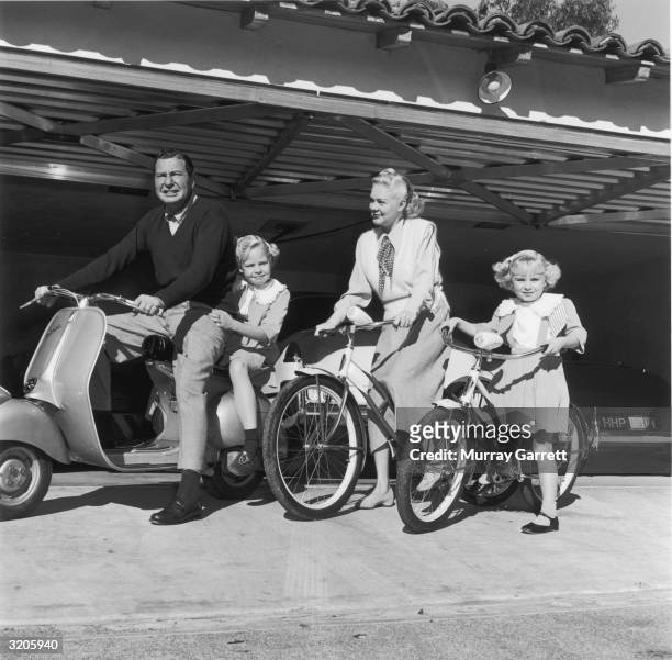 American actor and bandleader Phil Harris rides a moped as his wife, American actor and singer Alice Faye, and their two daughters, Alice and...