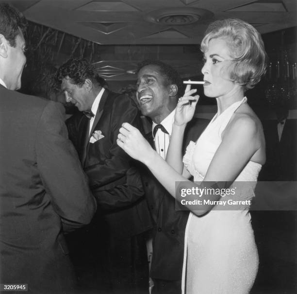 American actor Tony Curtis speaks with entertainers Dean Martin and Sammy Davis Jr. , as Curtis' wife, Janet Leigh, smokes a cigarette, at a Thalians...