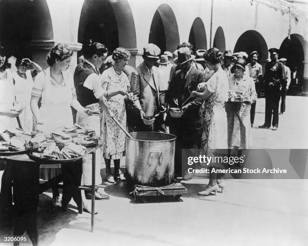 Unemployed men receiving soup and slices of bread in an outdoor breadline during the Great Depression, Los Angeles, California. Some women serve the...