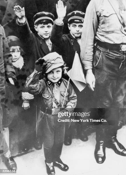 Full-length image of three children saluting from a crowd while standing at a curb during a National Socialistic Youth March in Berlin, Germany. A...