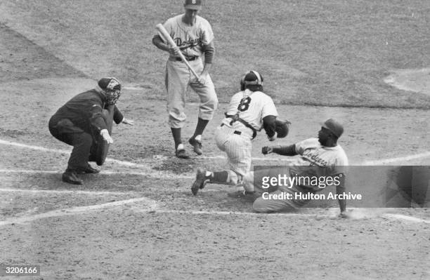 American baseball player Jackie Robinson, of the Brooklyn Dodgers, stealing home plate during the World Series game against the New York Yankees, New...