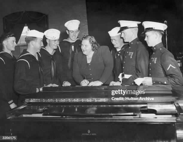 American vocalist Kate Smith smiles as she signs autographs for a group of uniformed sailors.