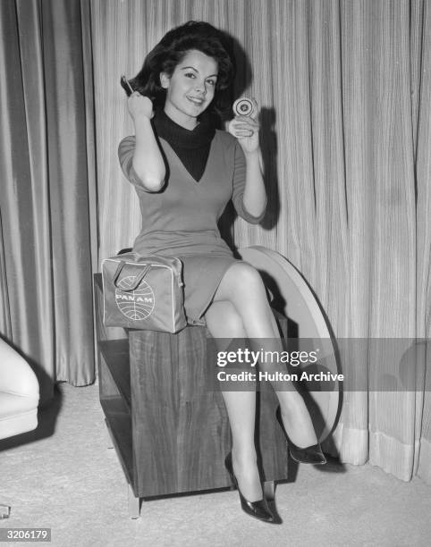 American actor and singer Annette Funicello smiles and brushes her hair using a compact prior to embarking on a European publicity tour for director...