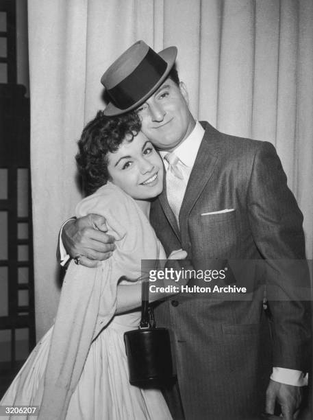 American actor Danny Thomas embraces American actor and singer Annette Funicello in front of a stage curtain, late 1950s. Thomas wears a jacket and a...
