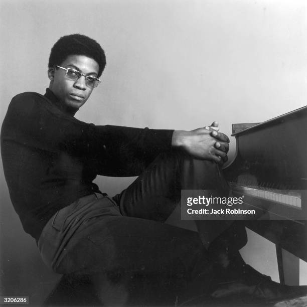Portrait of American jazz pianist and composer Herbie Hancock sitting at a piano with his hands clasped over one knee. He wears a dark turtleneck and...