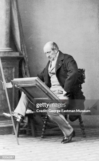 Full-length image of a middle-aged man looking at a framed painting while sitting in a studio.