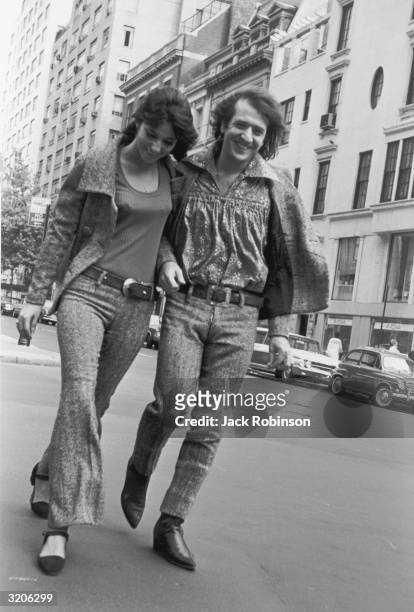 Married American pop/rock singing duo Sonny Bono and Cher walk arm-in-arm down the street, New York City. They wear herringbone tweed jackets and...