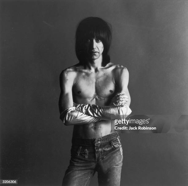 Studio portrait of American rock singer Iggy Pop, of the group the Stooges, posing barechested with his arms folded. He wears long satin gloves.