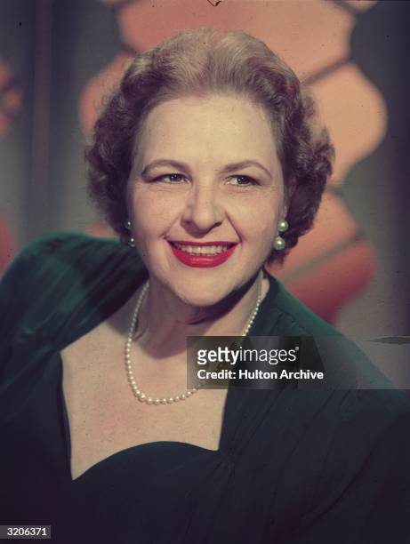 Headshot portrait of American vocalist Kate Smith smiling while wearing a dark dress and a string of pearls.