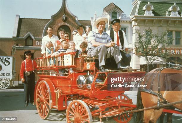 American animator and film studio founder Walt Disney sits in the front of a red, horsedrawn fire wagon, holding the reins, Disneyland, Anaheim,...